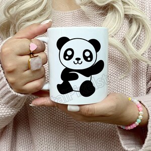 May include: White ceramic mug featuring a black and white cartoon panda design. The panda is waving and has large eyes.