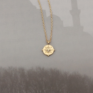 May include: A gold necklace with a compass pendant. The compass has a star in the center and four points.