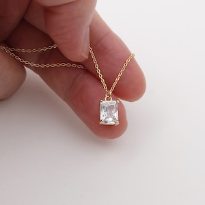 Puede incluir: Un collar de cadena dorada con un colgante de cristal transparente de forma cuadrada.