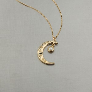 May include: A gold crescent moon necklace with a small pearl pendant. The moon is decorated with tiny stars.