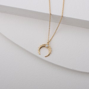 May include: A gold chain necklace with a crescent moon pendant featuring a white opal stone.