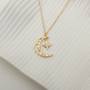 Puede incluir: Un collar de oro con un colgante de media luna y una pequeña estrella con un brillante transparente en el centro.