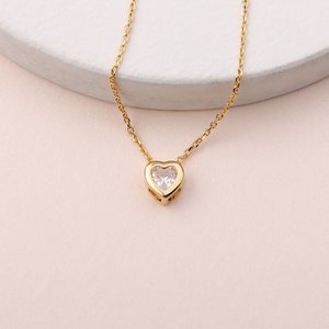 May include: A gold chain necklace with a small heart pendant featuring a clear cubic zirconia stone.