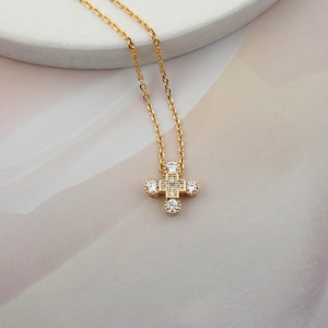 May include: A gold chain necklace with a small, sparkling cross pendant. The cross is made of clear cubic zirconia stones set in a gold frame.