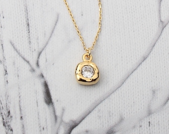 May include: A gold chain necklace with a small, square pendant featuring a clear, round gemstone.