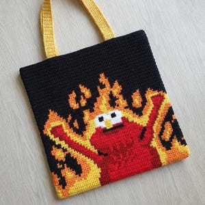 Puede incluir: Bolso tote de crochet negro hecho a mano con una imagen pixelada de un personaje rojo en llamas. El personaje tiene ojos blancos y una cara amarilla. El bolso tiene asas amarillas.