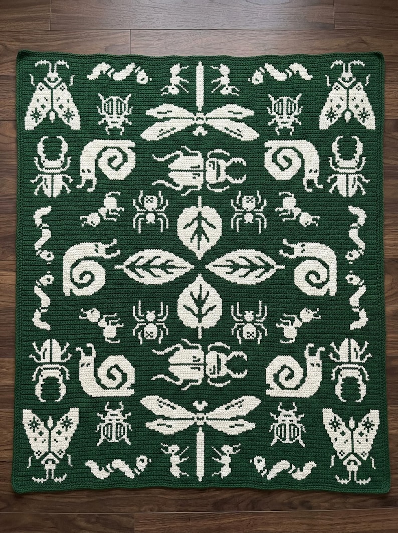 May include: A rectangular crochet blanket in dark green with a repeating white pattern of various insects, including dragonflies, beetles, snails, spiders, and caterpillars, arranged symmetrically around a central cluster of four leaves.