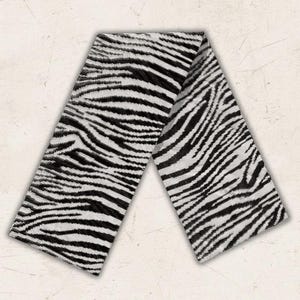 Puede incluir: Una bufanda larga y rectangular con un patrón de rayas de cebra en blanco y negro de alto contraste. La tela muestra un diseño de estampado animal consistente y repetitivo que cubre toda la superficie del accesorio de extremo a extremo.