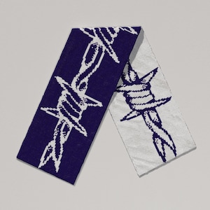 Könnte beinhalten: Gestrickter Schal mit einem sich wiederholenden weißen Stacheldrahtmuster auf marineblauem und cremefarbenem Hintergrund. Der Schal ist gefaltet und zeigt die Struktur des Stoffes. Das Design ist ein auffälliges, grafisches Statement.