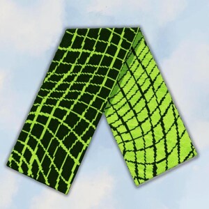 Könnte beinhalten: Ein rechteckiger Strickschal mit einem kontrastreichen geometrischen Gittermuster. Eine Seite zeigt einen schwarzen Hintergrund mit einem leuchtend lindgrünen Gitter, während die Rückseite einen lindgrünen Hintergrund mit einem schwarzen Gittermuster aufweist.