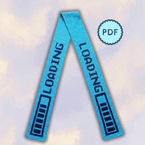 Puede incluir: Una cinta tejida de color azul brillante doblada en forma de V invertida. La cinta presenta un texto bordado en azul oscuro que dice LOADING seguido de un gráfico de barra de carga que consta de cinco segmentos rectangulares a cada lado.