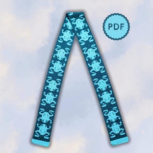 Pode incluir: Uma tira de tecido longa e estreita com um padrão repetitivo de sapos pixelizados em azul claro sobre um fundo azul-petróleo escuro. A tira está dobrada em forma de V invertido, com extremidades azul-claras. Um círculo recortado azul-claro com o texto PDF.
