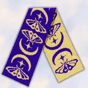 May include: A long rectangular knit scarf featuring a repeating pattern of moths, crescent moons, and four-pointed stars. The scarf displays a two-tone colour scheme, with one side showing yellow motifs on a deep blue background and the reverse side showing blue motifs on a yellow background.