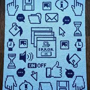 Könnte beinhalten: Eine hellblaue Häkeldecke mit einem dunkelblauen, pixeligen Muster aus Computer-Interface-Symbolen, darunter Cursor, Disketten, Ordner, Umschläge, Sanduhren und ein zentrales Fehlerfenster mit dem Text ERROR und OK.