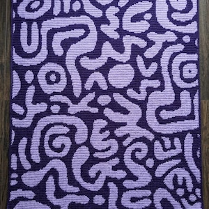 May include: A handmade crochet blanket featuring a repeating abstract design in shades of purple and lavender. The blanket's pattern consists of swirling, organic shapes, creating a visually engaging texture. This cozy blanket is perfect for home decor.
