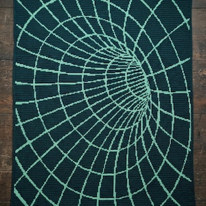 May include: A dark teal crocheted blanket with a light teal geometric design. The design creates the illusion of a tunnel or vortex. The blanket is rectangular and appears to be handmade.
