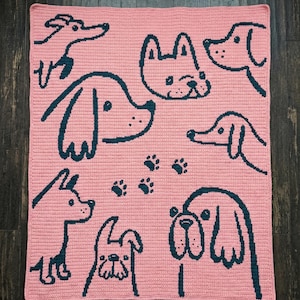 Puede incluir: Una manta rosa tejida a ganchillo con dibujos lineales en azul oscuro de varias razas de perros y huellas de patas. La manta es rectangular y tiene un aspecto texturizado.