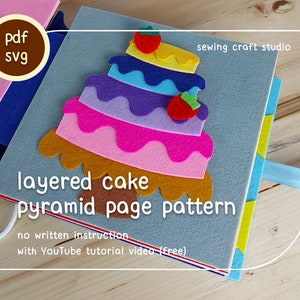 Pode incluir: Um livro de feltro feito à mão com um design de bolo em camadas. O bolo é feito de camadas de feltro coloridas e coberto com morangos. O livro é cinza com uma fita azul e o texto "layered cake pyramid page pattern".