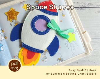 Puede incluir: Una página de libro sensorial de fieltro con un cohete blanco, detalles azules y rojos, y una llama amarilla y naranja. La página se titula "Space Shapes" e incluye una estrella dorada brillante y una cinta verde. Diseñado por Buni de Sewing Craft Studio.