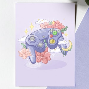 Puede incluir: Un mando de GameCube morado con flores rosas y blancas, nubes y estrellas sobre un fondo morado claro. El texto "GameCube" está escrito en el mando.