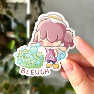 Op de afbeelding: Een sticker met een stripfiguur met roze haar en een witte hoed, die bellen blaast. Het personage draagt een paarse jurk en gele schoenen. Het woord "BLEUGH" staat in het wit onderaan de sticker.