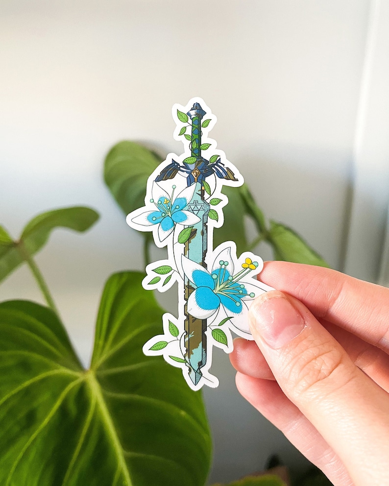 May include: A sticker featuring a stylized sword with blue and white flowers growing around it. The sword is blue and green with a gold hilt. The flowers are white with blue centers.