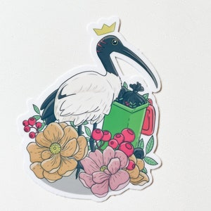 May include: A white ibis wearing a gold crown holds a green bin with a black bag inside. The ibis is surrounded by pink and yellow flowers and red berries.