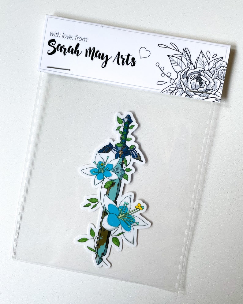 May include: A sticker featuring a blue and green sword with white flowers wrapped around it. The sticker is on a white background with a small heart and the text "with love, from Sarah May Arts".
