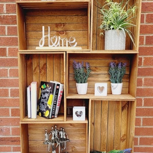 Puede incluir: Una estanter&iacute;a de madera con seis compartimentos, que presenta una variedad de art&iacute;culos decorativos, incluyendo plantas, libros y una escultura de metal. La estanter&iacute;a est&aacute; etiquetada como "Home" y tiene un estilo r&uacute;stico, de granja.