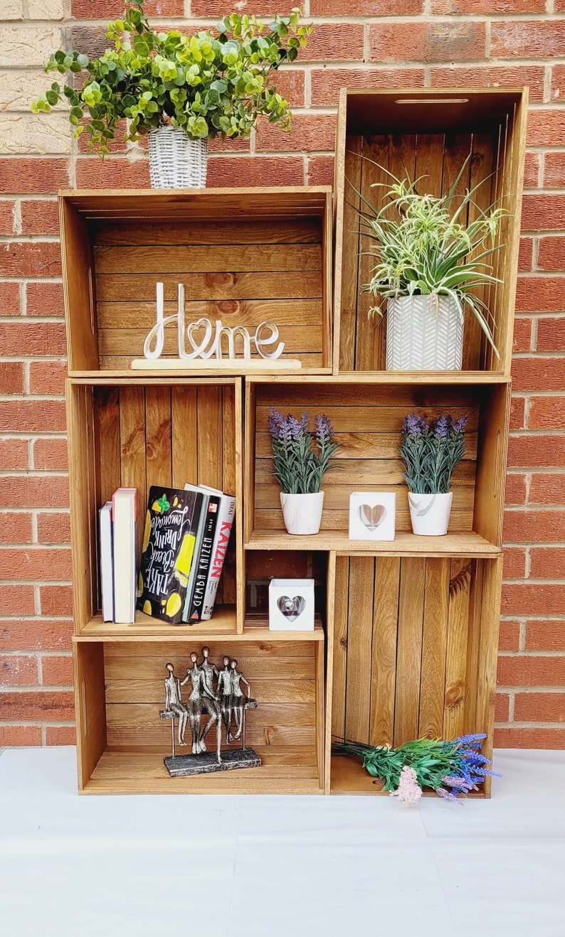 Puede incluir: Una estanter&iacute;a de madera con seis compartimentos, que presenta una variedad de art&iacute;culos decorativos, incluyendo plantas, libros y una escultura de metal. La estanter&iacute;a est&aacute; etiquetada como "Home" y tiene un estilo r&uacute;stico, de granja.