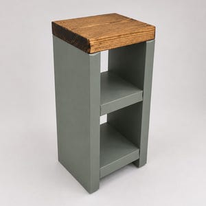 May include: A small, gray wooden side table with two shelves. The top is made of a stained, light brown wood. The table is a simple, modern design, suitable for a living room or bedroom. The table is approximately 28 inches tall.