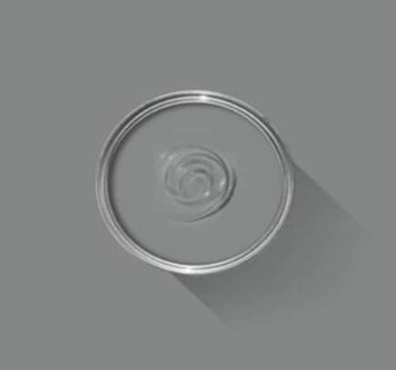 May include: An overhead view of an open can of gray paint. The paint has a swirl pattern in the center. The can is silver and sits on a gray surface, casting a shadow.