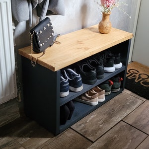 May include: A black wooden shoe rack with two shelves. The top shelf is made of light wood and has a black purse on it. The bottom shelf has several pairs of shoes, including black sneakers and brown sandals.