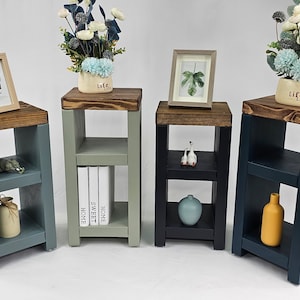 May include: Four wooden shelf units with different coloured paint finishes. The shelves are each decorated with small items, including a picture frame, books, a vase of flowers, and a small ceramic figurine. The shelves are all approximately 76 cm tall.