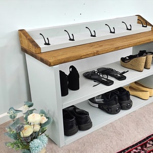 May include: White wooden shoe rack with two shelves and a top shelf with hooks. The rack is filled with shoes, including sneakers, sandals, and heels.