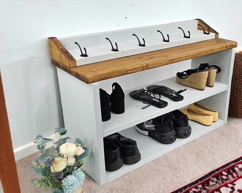 May include: White wooden shoe rack with two shelves and a top shelf with hooks. The rack is filled with shoes, including sneakers, sandals, and heels.