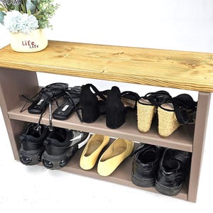 May include: A two-tiered wooden shoe rack with a light brown top and a gray base. The top shelf is made of reclaimed wood and has a natural finish. The bottom shelf is painted gray. The shoe rack is filled with various shoes, including sandals, sneakers, and flats.