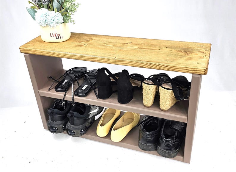 May include: A two-tiered wooden shoe rack with a light brown top and a gray base. The top shelf is made of reclaimed wood and has a natural finish. The bottom shelf is painted gray. The shoe rack is filled with various shoes, including sandals, sneakers, and flats.