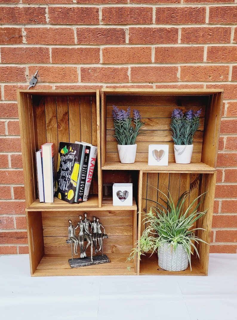 Puede incluir: Una estanter&iacute;a de madera con cuatro estantes, que presenta una escultura decorativa de cinco figuras, dos plantas en maceta y tres libros. La estanter&iacute;a est&aacute; hecha de madera reciclada y tiene un aspecto r&uacute;stico.