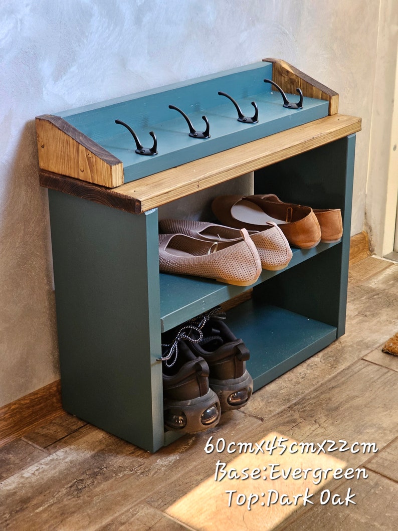 Op de afbeelding: Een schoenenrek met twee planken en een bovenste plank met haken. De basis is geverfd in evergreen groen en de bovenkant is donker eiken. Het rek meet 60 cm x 45 cm x 22 cm.