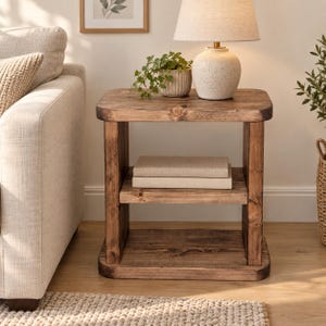 May include: A rectangular side table crafted from dark stained wood with a smooth top surface, a middle shelf holding two stacked books, and a solid base. The table features visible wood grain patterns and rounded corners on the top and bottom.