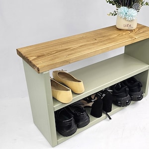 May include: A light green wooden shoe rack with two shelves. The top shelf is made of natural wood and has a light brown finish. The rack is holding a pair of black shoes, a pair of brown shoes, and a pair of black heels.