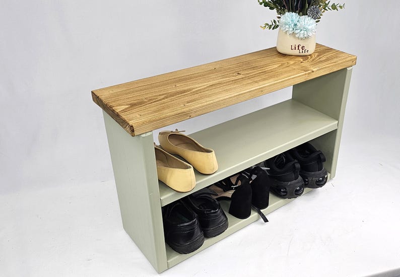 May include: A light green wooden shoe rack with two shelves. The top shelf is made of natural wood and has a light brown finish. The rack is holding a pair of black shoes, a pair of brown shoes, and a pair of black heels.