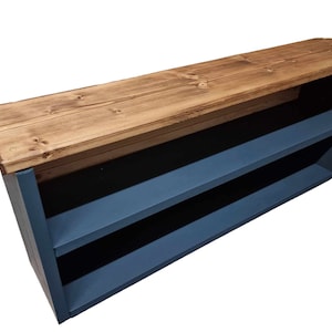 May include: A wooden shelf unit with two shelves painted a dark blue color. The top shelf is made of natural wood and is unfinished. The shelf unit is angled and has a rustic look.