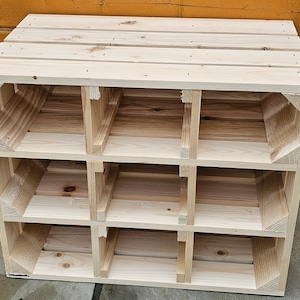 May include: A light-colored, unfinished wooden storage unit with nine cubby holes. The unit is constructed from wooden planks and has a rectangular shape. The cubbies are arranged in three rows of three. The unit is suitable for organizing items.