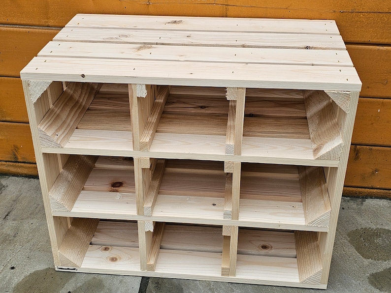 May include: A light-colored, unfinished wooden storage unit with nine cubby holes. The unit is constructed from wooden planks and has a rectangular shape. The cubbies are arranged in three rows of three. The unit is suitable for organizing items.