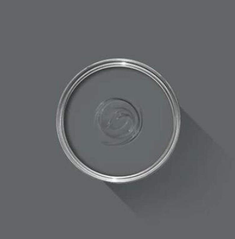 May include: An overhead view of a partially open, round, silver paint can filled with gray paint. The paint has a swirl pattern in the center. The can casts a shadow on the gray surface.