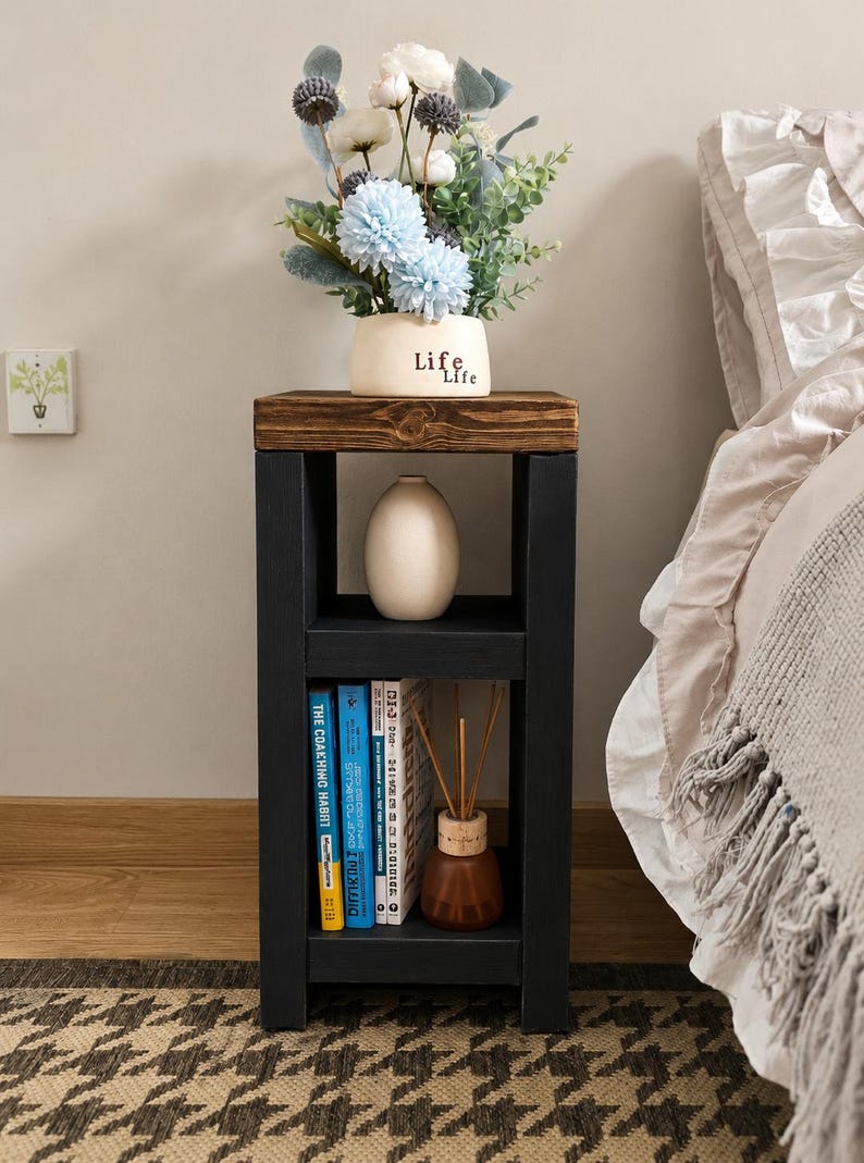 May include: A black and brown wooden side table with a shelf, holding books, a vase, and a diffuser. The top shelf displays a vase with blue and white flowers. The vase has the word "Life" on it.