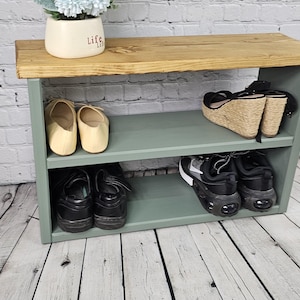 May include: A green wooden shoe rack with two shelves. The top shelf has a wooden top and the bottom shelf has a pair of sandals, a pair of sneakers, and a pair of flats.