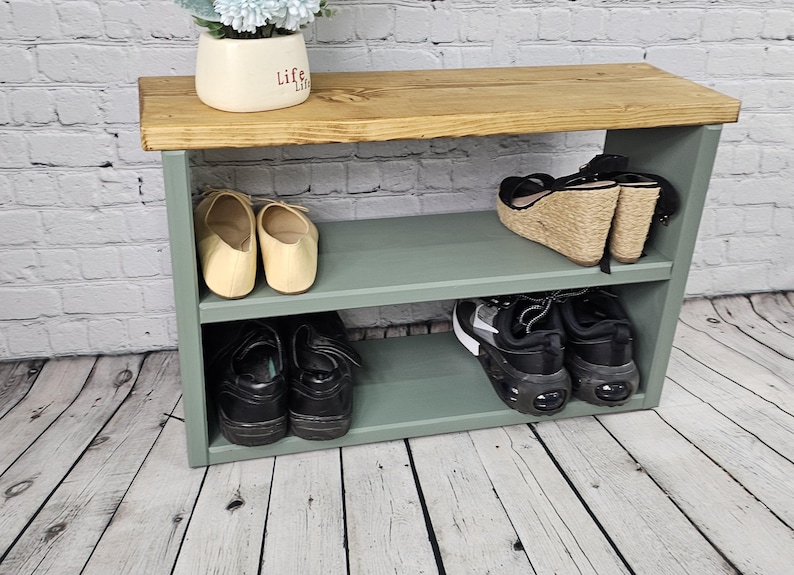 May include: A green wooden shoe rack with two shelves. The top shelf has a wooden top and the bottom shelf has a pair of sandals, a pair of sneakers, and a pair of flats.
